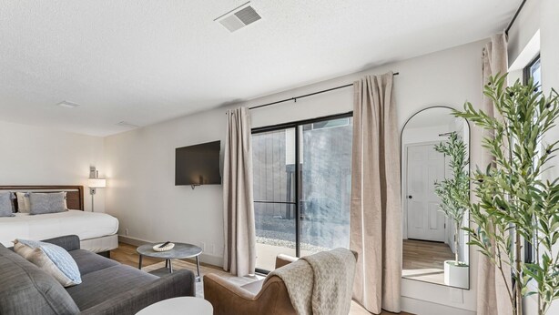 A modern hotel room with a bed, sofa, armchair, small round table, and a large window with curtains. - Extended Stay Fully Furnished Studios At The Cass (Omaha)