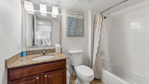 A bathroom with a granite countertop sink, a toilet, and a shower with a curtain. - Extended Stay Fully Furnished Studios At The Cass (Omaha)