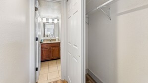 A hallway leading to a bathroom with a white door, a mirror, and a vanity with a sink. - Extended Stay Fully Furnished Studios At The Cass (Omaha)