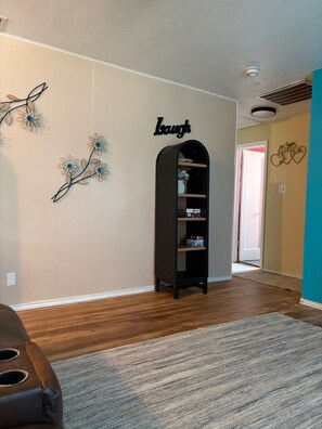 A room with a bookshelf, a wall-mounted sign, and a door leading to another room.