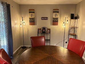 Un comedor con una mesa redonda de madera, sillas rojas, una barra de café y luminarias fijadas a la pared.