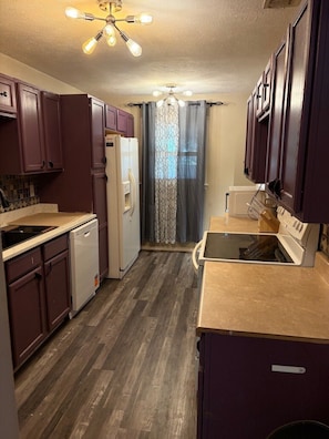 A compact kitchen with wooden cabinets, a dishwasher, a refrigerator, and a stove.