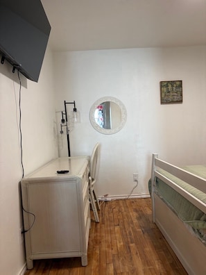 A small, tidy room with a bed, a desk, a chair, a mirror, and a television mounted on the wall.