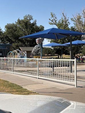 Zona de juegos vallada con fuentes de agua y mesas de picnic.