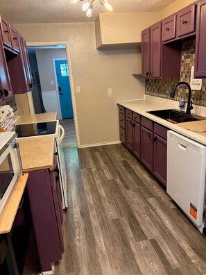 Cocina con piso de madera, lavavajillas, microondas y armarios.