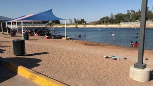 Ein Strand mit einer überdachten Sitzgelegenheit, einem Mülleimer und einer Betonbarriere.