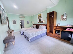 Quarto com duas camas, um banco de madeira, uma mesinha, um espelho e ar condicionado fixado na parede.