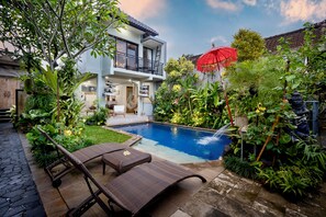 Uma casa moderna com piscina, cercada por vegetação exuberante e um guarda-sol vermelho.