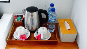 Una bandeja con una botella de agua, una caja de pañuelos, una cafetera y dos tazas con una flor.
