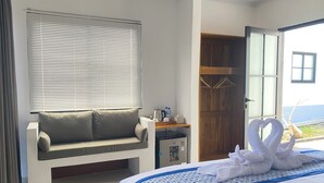 Habitación de hotel con una cama, zona de estar, armario de madera y ventana con persianas.
