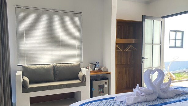 Habitación de hotel con una cama, zona de estar, armario de madera y ventana con persianas.