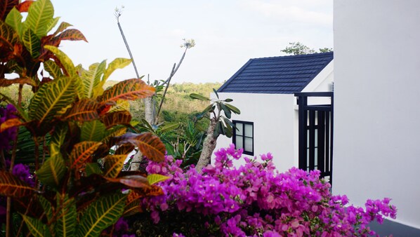 A white building with a dark roof, surrounded by lush greenery and purple flowers. - Penida Cabins (Penida Island)