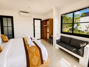 A hotel room with a bed, a sofa, a wardrobe, and a window with a view. - Penida Cabins (Penida Island)