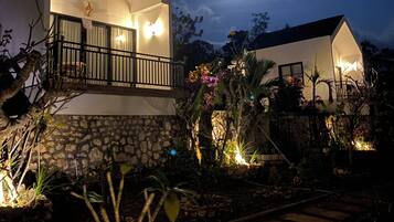 Una casa moderna con balcón, base de piedra y un jardín con plantas y un camino.