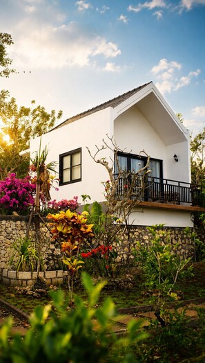 A white building with a balcony, surrounded by lush greenery and flowering plants. - Penida Cabins (Penida Island)