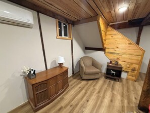 Ein Zimmer mit einer Holztreppe, einem Schrank, einem Stuhl und einem kleinen Tisch mit einer Lampe.