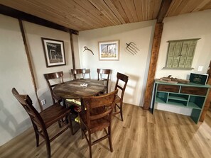 Ein Essbereich mit einem runden Holztisch, umgeben von Stühlen, einer Holzzieldecke und einem grünen Schrank mit Schubladen.