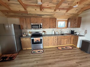 A kitchen with wooden cabinets, stainless steel appliances, and a window. - Restored 1800s Barn Retreat 2 bd • 1.5 Bath Between Kalispell & Whitefish (Kalispell)