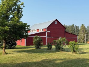 A red barn with a metal roof, surrounded by green grass and trees. - Restored 1800s Barn Retreat 2 bd • 1.5 Bath Between Kalispell & Whitefish (Kalispell)