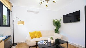 Ett modernt vardagsrum med en soffa, ett soffbord, en golvlampa, en tv och en krukväxt.