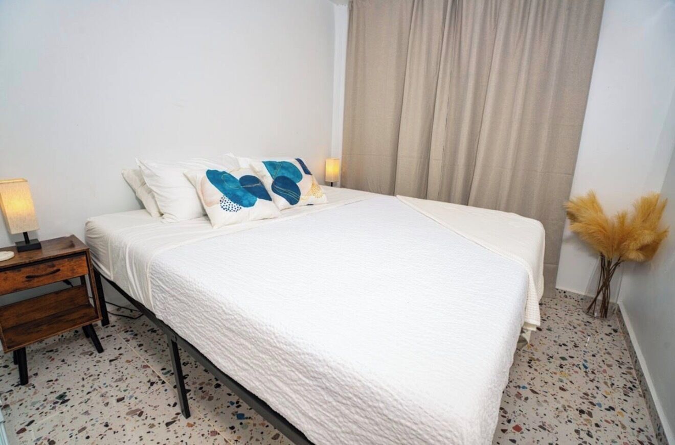 A bedroom with a bed, a bedside table, a lamp, and a wall-mounted light.