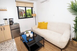 Een gezellig, compact ingerichte ruimte met een bank, een klein tafeltje, een kitchenette en een raam met uitzicht.