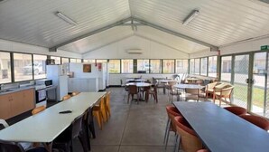 Un espacio de comedor techado con mesas y sillas, una zona de cocina y ventanas amplias.