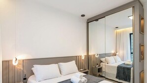 A hotel room with a large bed, a bedside table, a nightstand, a mirror, and a wall-mounted light fixture. - Ap With sea View Near the Beach in Itapema Alx0803 (Itapema)