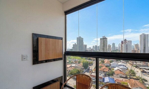 Ein Zimmer mit einem großen Fenster, einem gerahmten Bild an der Wand und einem Korbstuhl.