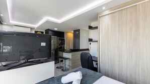 A compact hotel room with a bed, a desk, a chair, a television, and a kitchenette. - Apt. in Condo. w/ Heated Pool Sak1138 (Curitiba)