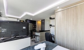 A compact hotel room with a bed, a desk, a chair, a television, and a kitchenette. - Apt. in Condo. w/ Heated Pool Sak1138 (Curitiba)