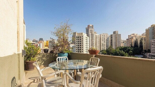 Ein Tisch mit Glasplatte und Stühlen auf einem Balkon mit Blick auf eine Skyline und hohe Gebäude.