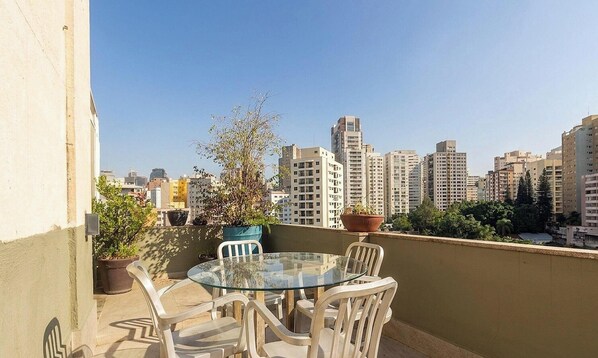 A glass-top table with chairs on a balcony overlooking a cityscape with high-rise buildings. - Apt. w/ Balcony in Bela Vista Paz0122 (São Paulo)