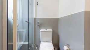 Ein Badezimmer mit Duschkabine aus Glas, Toilette und Mülleimer.