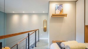 A modern hotel room with a wooden staircase, a bed with rolled towels, a wall-mounted mirror, and a decorative piece above the bed. - Apt. w/ Balcony in Condo. 500m From Beach Lan0204 (Florianópolis)