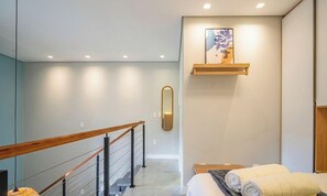 Ein modernes Hotelzimmer mit einer Holztreppe, einem Bett mit aufgerollten Handtüchern, einem Wandspiegel und einem dekorativen Gegenstand über dem Bett.