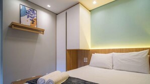 A hotel room with a bed, a headboard, a wall-mounted shelf with a picture, and a bedside table with towels. - Apt. w/ Balcony in Condo. 500m From Beach Lan0204 (Florianópolis)