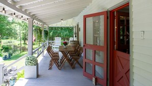 Un porche cubierto con una mesa y sillas de comedor, una puerta roja y vistas a un jardín.