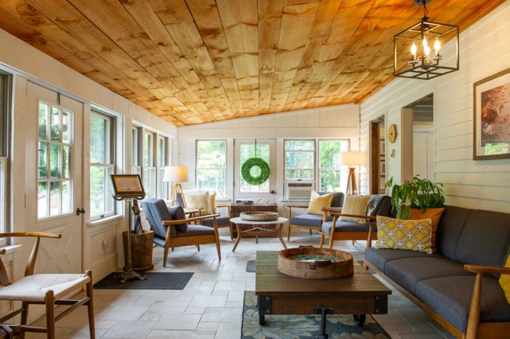 A cozy living room with wooden ceiling, large windows, and a fireplace.