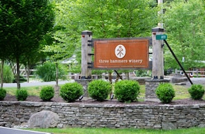 Placa de 'Three Hammers Winery' com um muro de pedra e pequenos arbustos à frente.