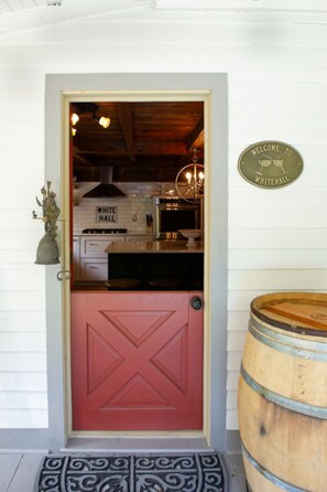 Uma porta vermelha com uma placa 'White Hall', uma placa de boas-vindas e um barril de madeira no alpendre.