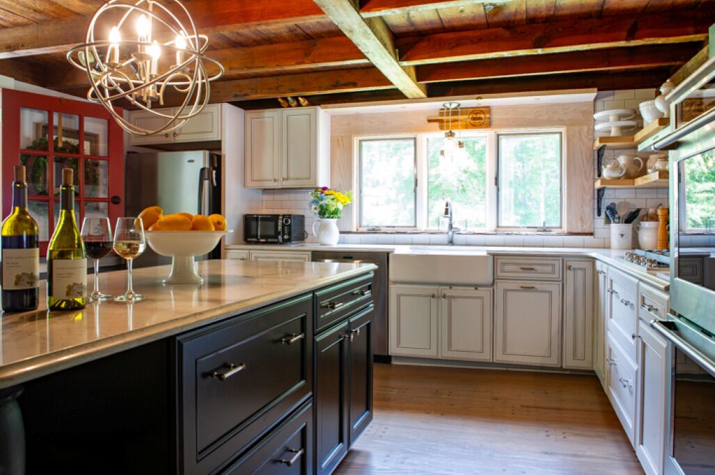 A kitchen with white cabinets, a wooden ceiling, and a central island with a bowl of fruit and wine bottles.