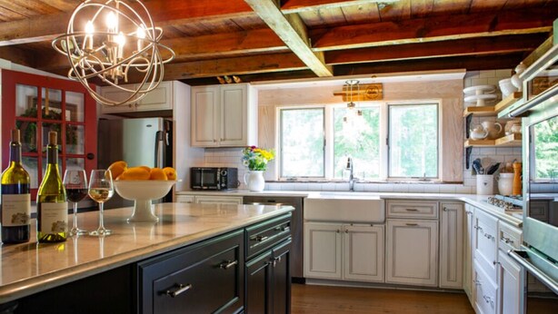 Una cocina con armarios blancos, techo de madera y una isla central con un cuenco de fruta y botellas de vino.