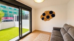 A living room with a grey sofa, a wall-mounted decorative piece, a sliding glass door leading to a balcony with artificial grass, and a wooden floor. - Villa Carinn Sella - Ribadesella - Beach 2 km away (Ribadesella)