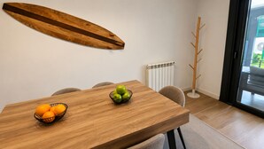 A dining area with a wooden table, two chairs, a fruit bowl with apples and oranges, and a wooden surfboard on the wall. - Villa Carinn Sella - Ribadesella - Beach 2 km away (Ribadesella)