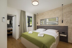 Une chambre d’hôtel moderne, avec un lit, un tableau, une table de chevet et une salle de bain visible à travers une porte ouverte.