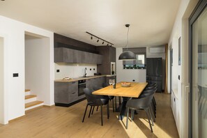 Une cuisine moderne avec un coin repas, comprenant une table en bois, des chaises noires et un four encastré.