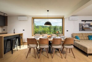 A modern kitchen with a dining area, a large window with a view of greenery, and a contemporary living space with a sofa and a painting. - Villa Mochi (Istria - Pićan) (Pićan)