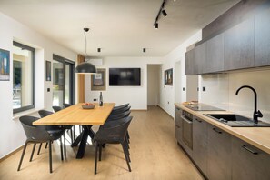Eine moderne Küche mit einem Holzesstisch, schwarzen Stühlen, einem großen Flachbildfernseher und einem eingebauten Backofen.