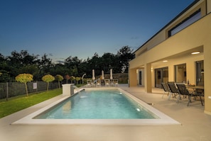 Ein rechteckiger Swimmingpool mit Wasserfall, umgeben von einer Terrasse mit Sitzgelegenheiten im Freien und einer Rutsche.
